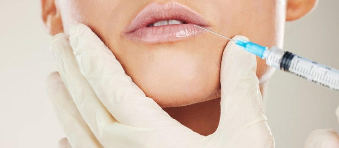 Skincare, mouth and collagen, woman with injection in lips from healthcare professional, anti aging treatment in studio. Beauty, needle and model with facial lip filler syringe on white background.