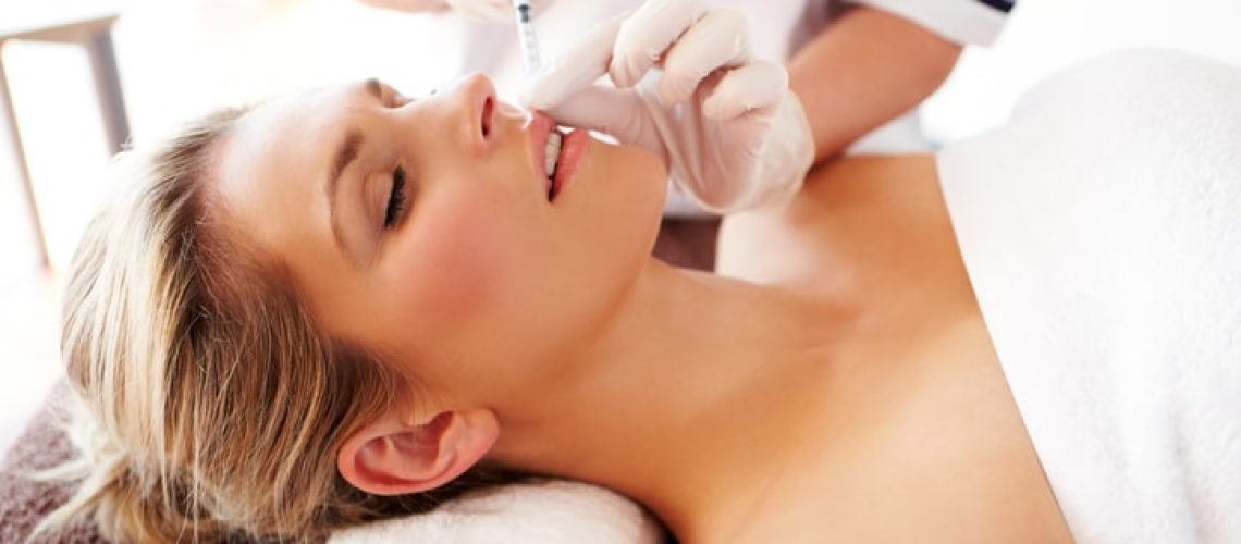 Young woman lies on her back while getting an injection to enlarge her lips.